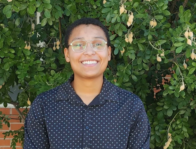 Woman with short hair and glasses pictured in front of greenery